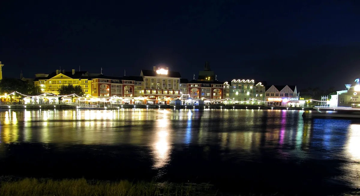Fachadas iluminadas do Disney’s BoardWalk à noite, com reflexos na água.