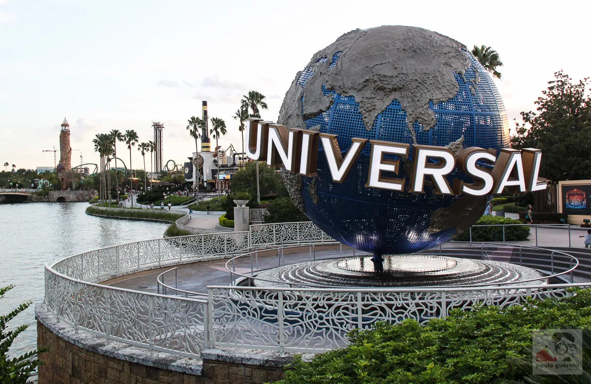 Globo azul com a palavra Universal, junto ao lago e às palmeiras do Universal Orlando.